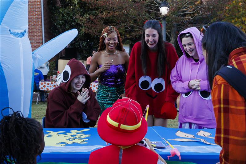 UWG Students standing behind a table wearing fun halloween costumes and handing out candy to children trick-or-treating.