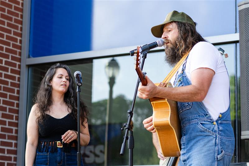 Two singers, one playing guitar, standing in front of the Campus Center.