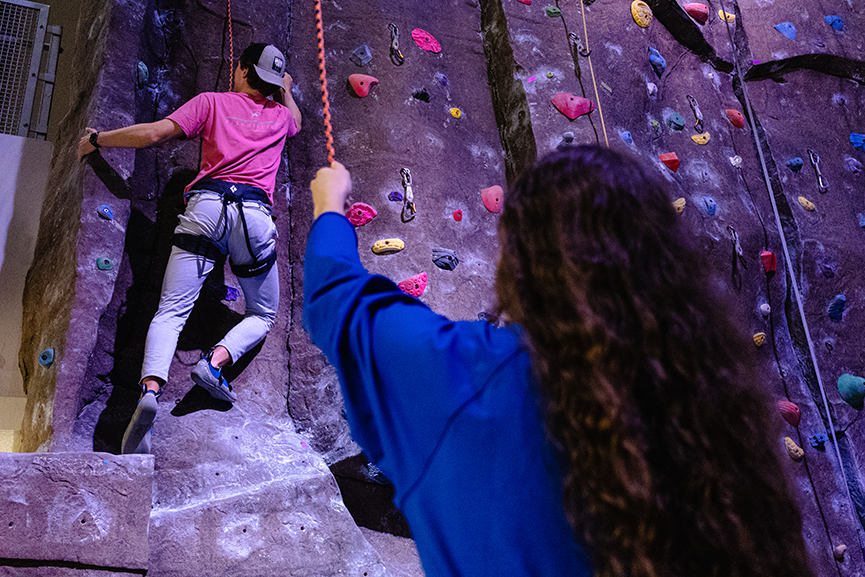 students climbing rock wall while getting belayed by UREC staff