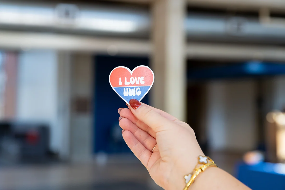 student holding an I LOVE UWG heart sticker