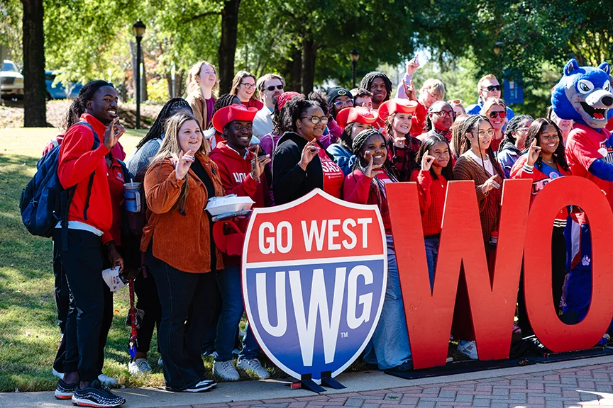 Students gathered around campus signage posing for a picture.