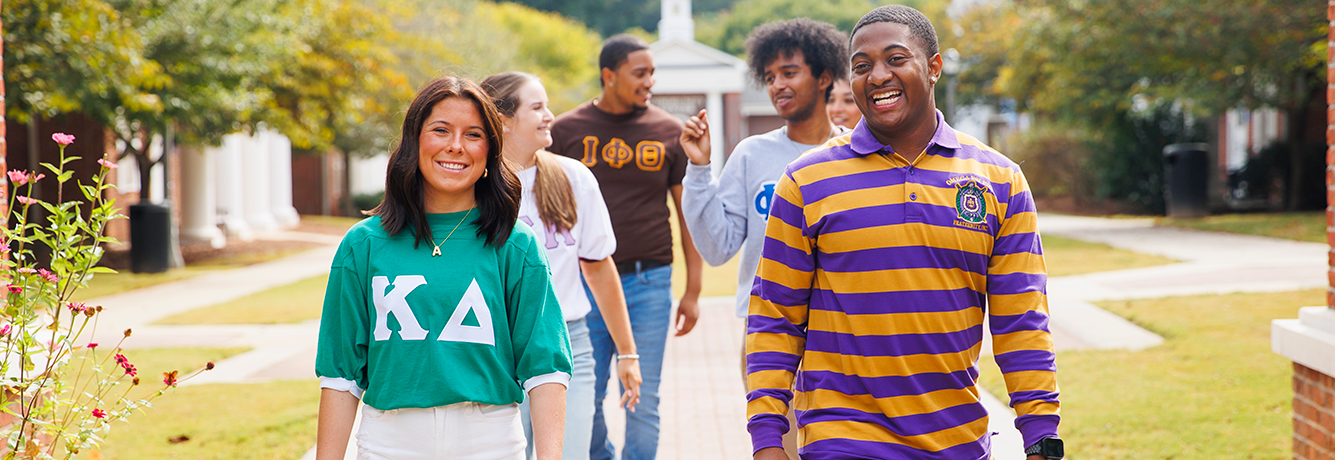 Greek students walking and smiling on campus wearing their letters