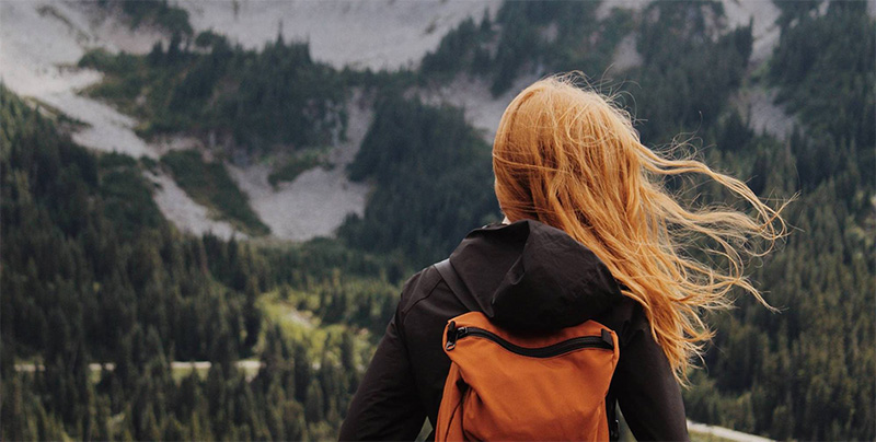 back of female head with backpack, mountains in backdrop
