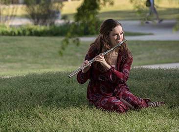 student playing flute seated on grass