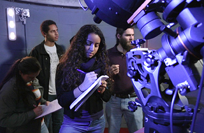 student in observatory looking through telescope