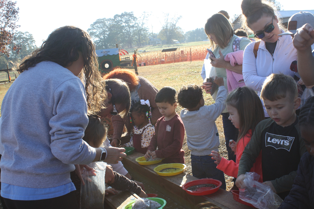 learning image of kids standing outside in a line with sand in plates. they are learning about the sand.