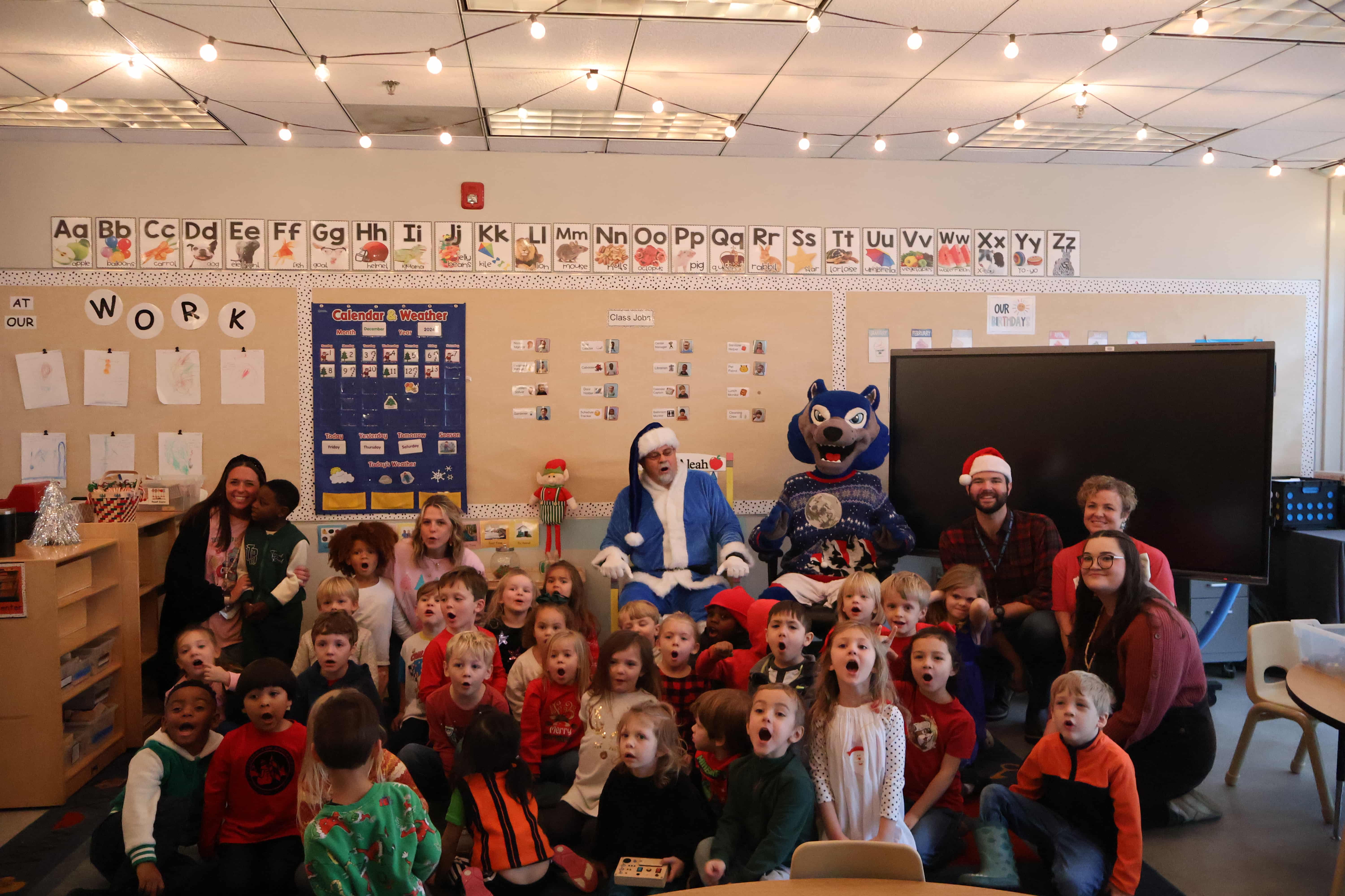 Pre-K students with the College of Education Dean dressed in a UWG blue santa suit. They are saying "ho ho ho" to the camera.