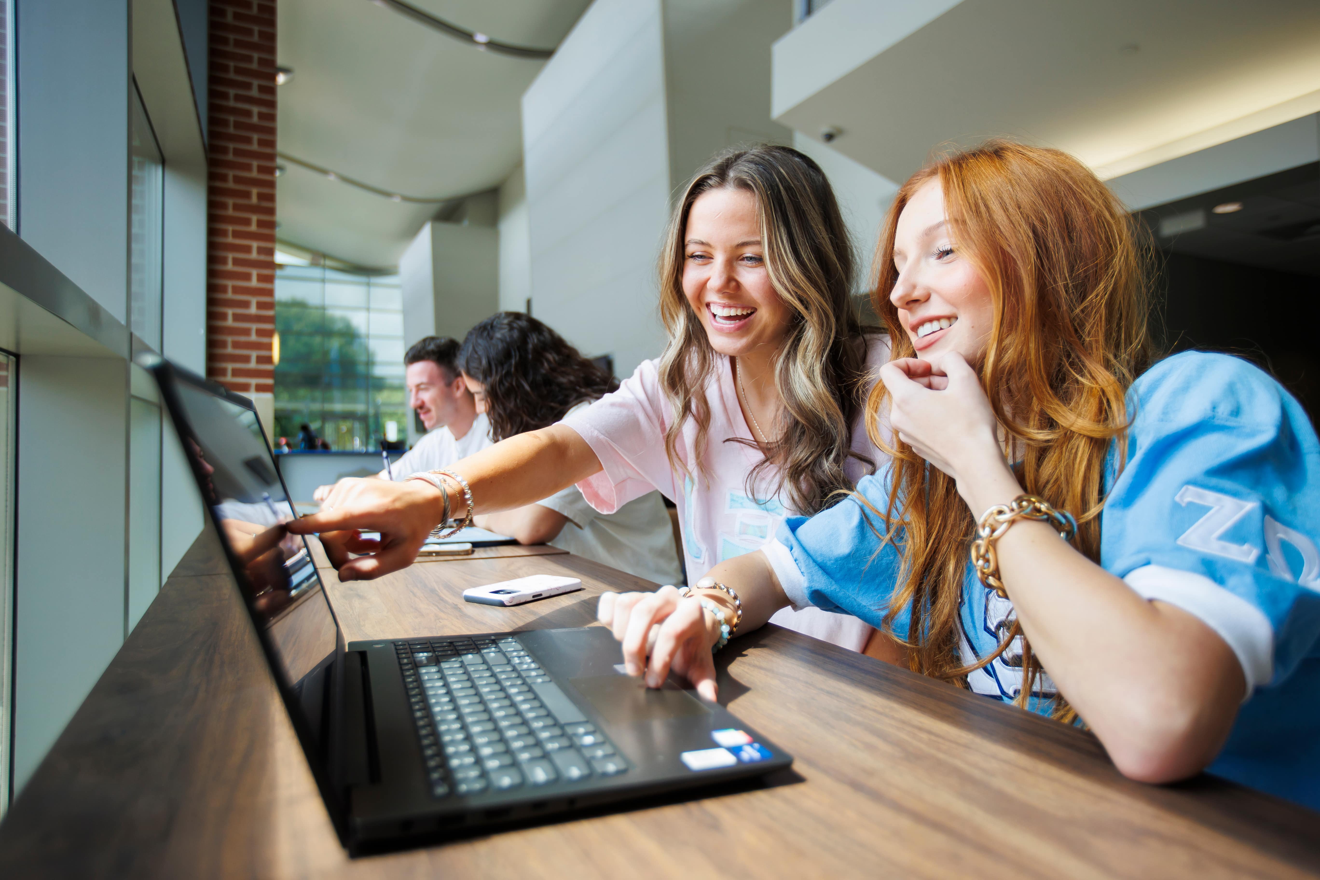 Two students pointing at a laptop and looking at the screen.