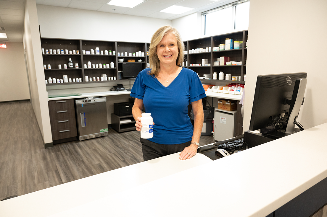 pharmacist Jennifer Daniel smiling behind pharmacy counter holding pill bottle