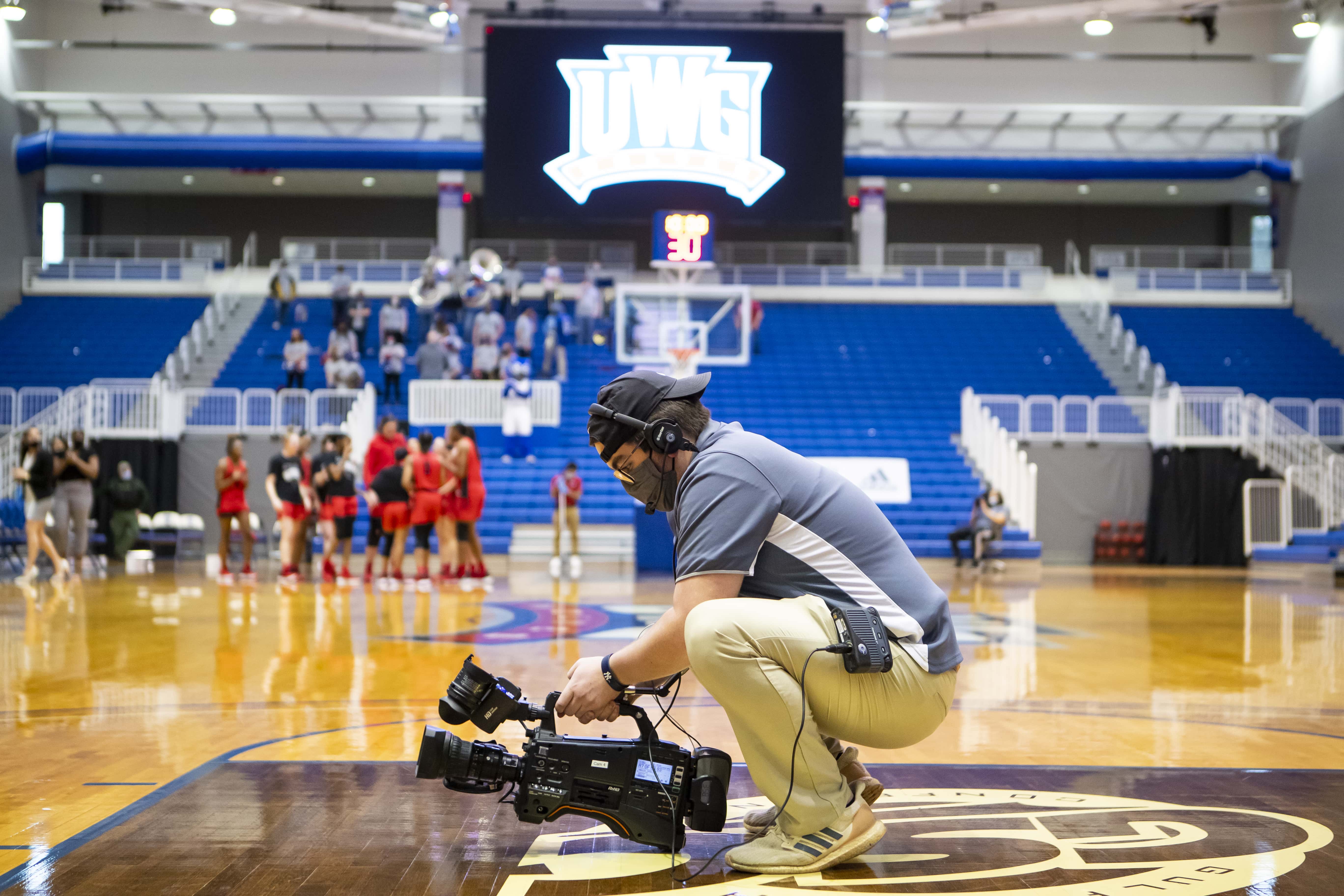 Camera man standing in a squat with a camera on the basketball field.