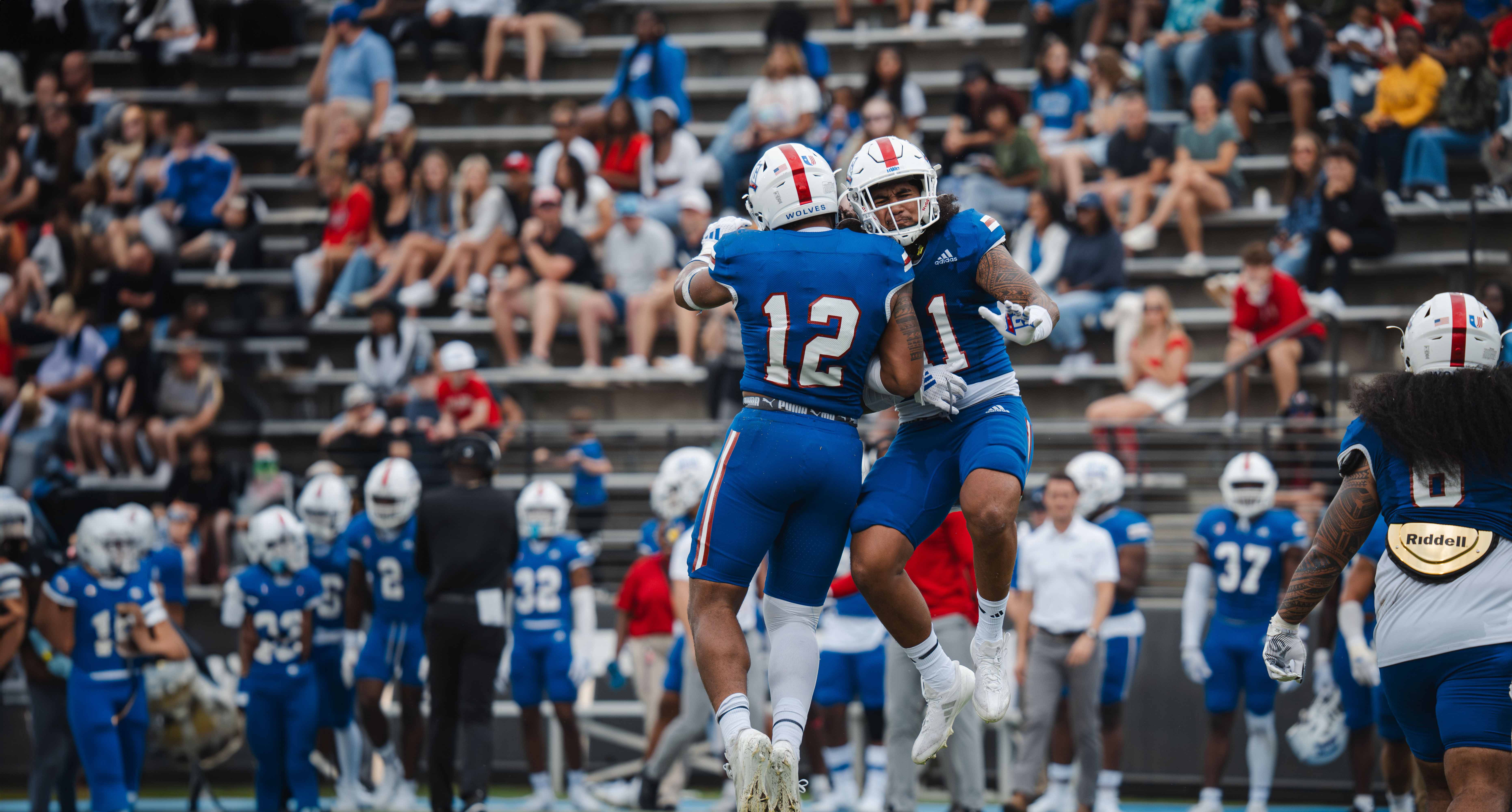 UWG football players jumping for a chest bump on the field.