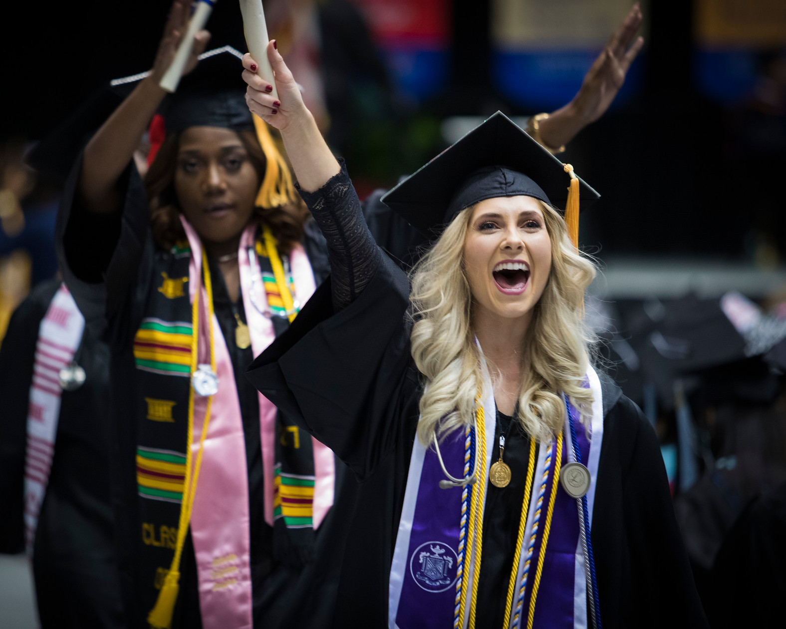 two women (one White and one African-American) walking with their diplomas